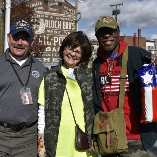 A volunteer at the Smiles for Our Heroes events poses with two veterans.