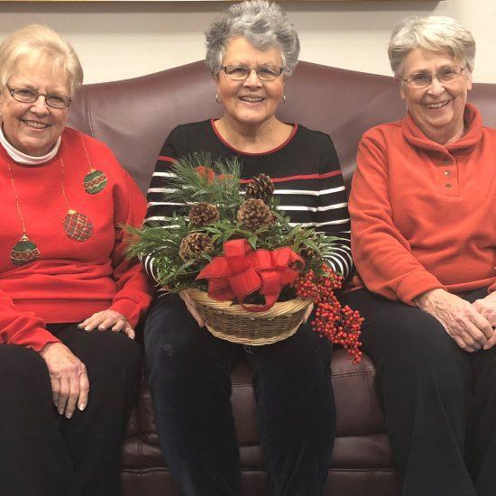 Photo of three members of the Bridgewater Garden Club sitting on a couch holding a holiday arrangement.