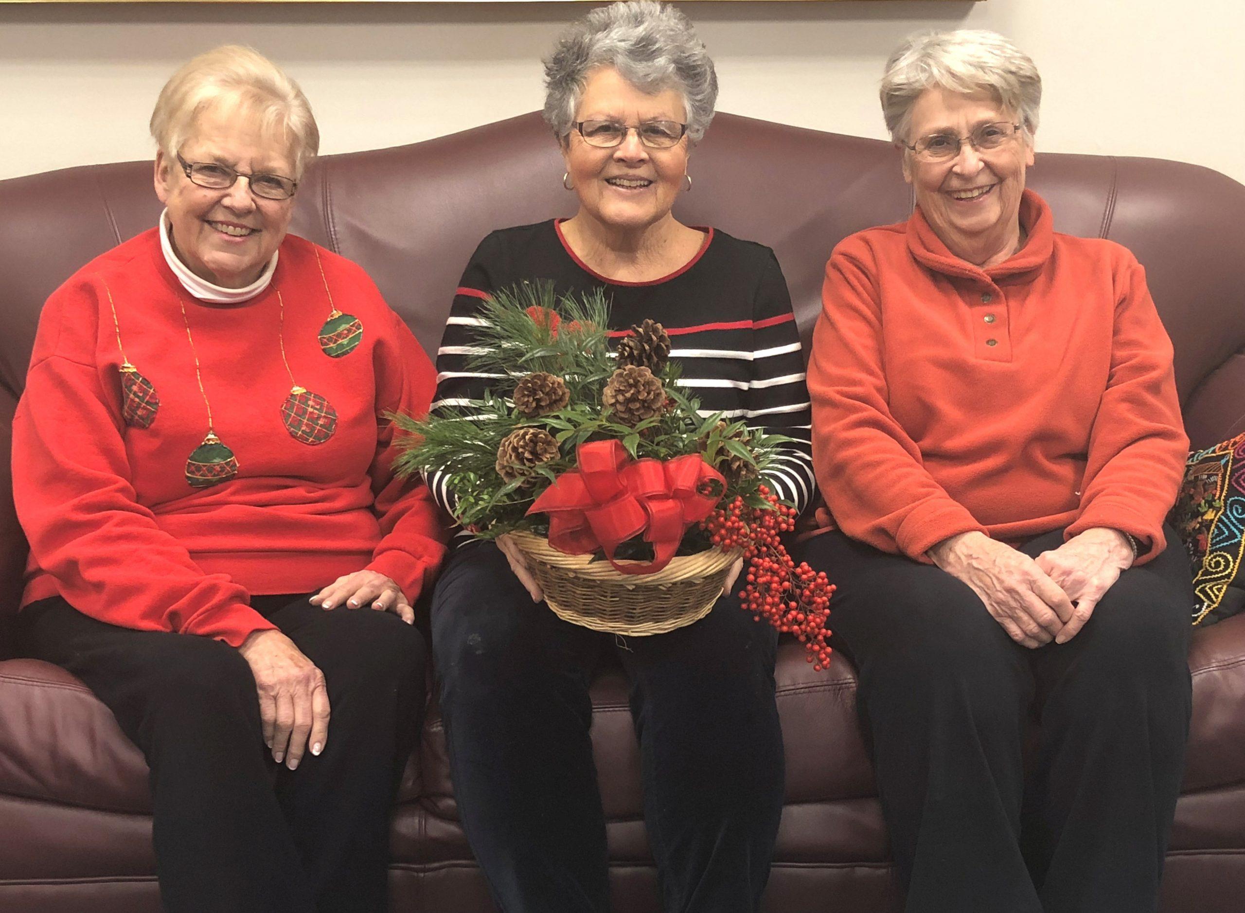 Photo of three members of the Bridgewater Garden Club sitting on a couch holding a holiday arrangement.