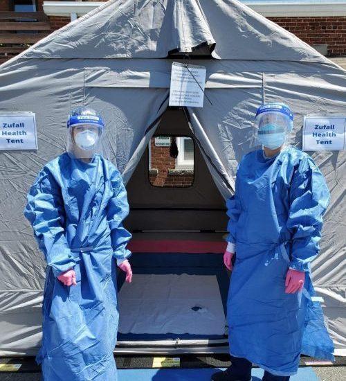 Photo of two medical personnel dressed in personal protective equipment standing in front of a medical tent