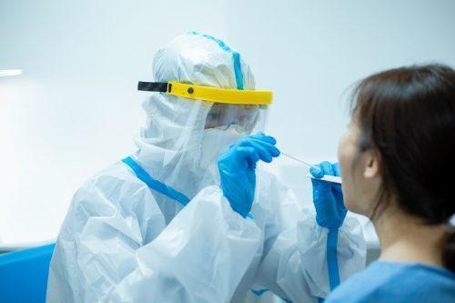 A doctor wearing full Personal Protective Equipment tests a female patient for Coronavirus