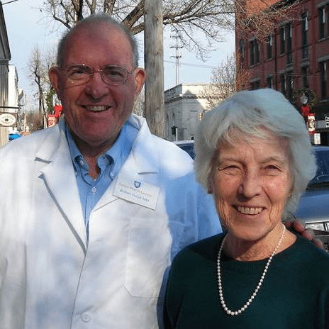 Two people standing outside smiling, one of whom is wearing a white doctor's coat