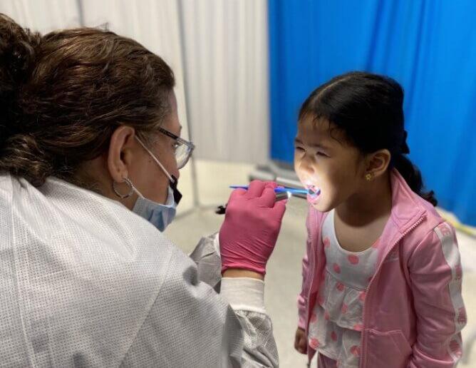 A dentist wearing a protective face masks conducts an oral health screening for a school-aged child