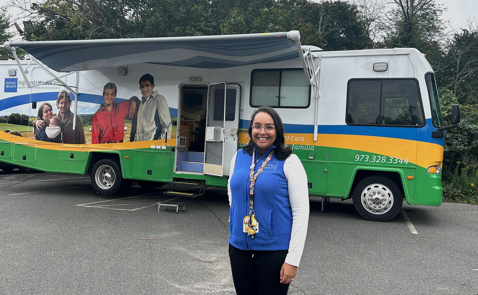 Person wearing blue vest standing in front of a multi-color medical van in a school parking lot