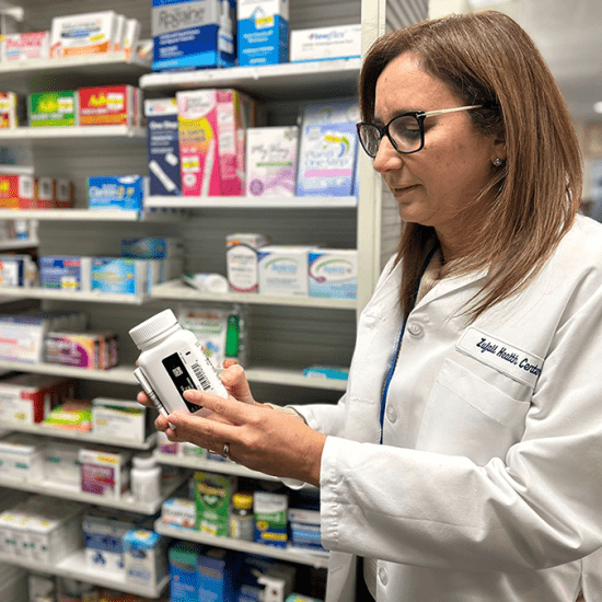 Pharmacist wearing a white coat holding a pill bottle in a pharmacy surrounded by medications
