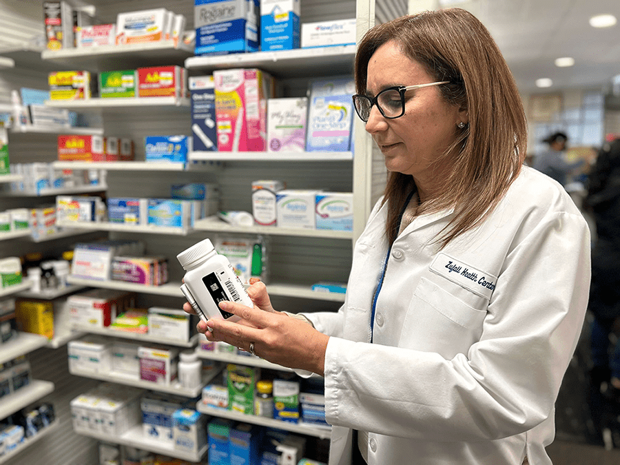 Pharmacist wearing a white coat holding a pill bottle in a pharmacy surrounded by medications