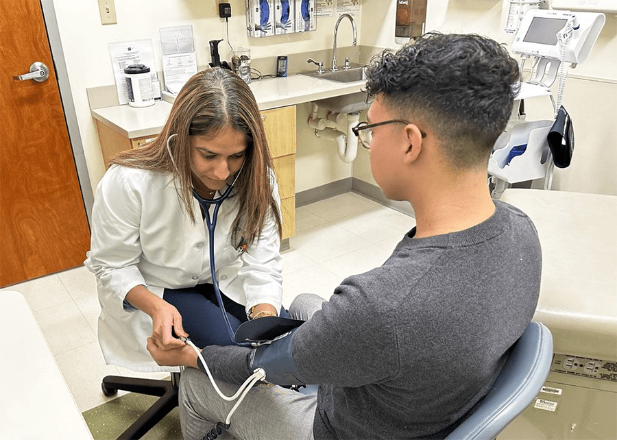 A health care provider measures a patient's blood pressure in a medical exam room.