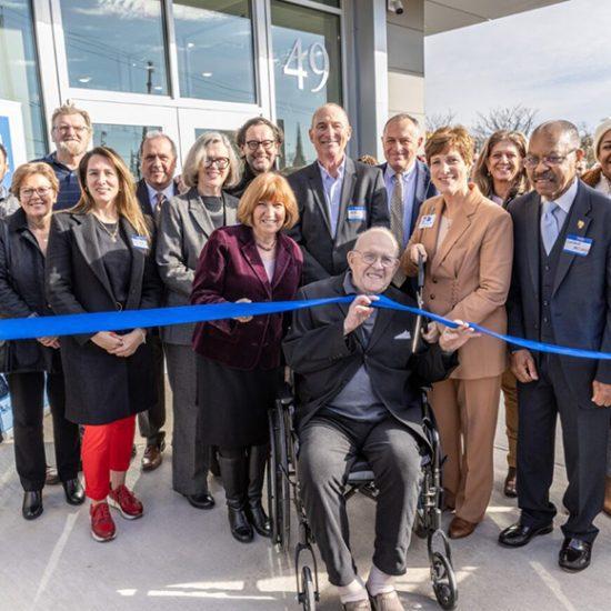 Group of people cutting a ribbon in front of a building