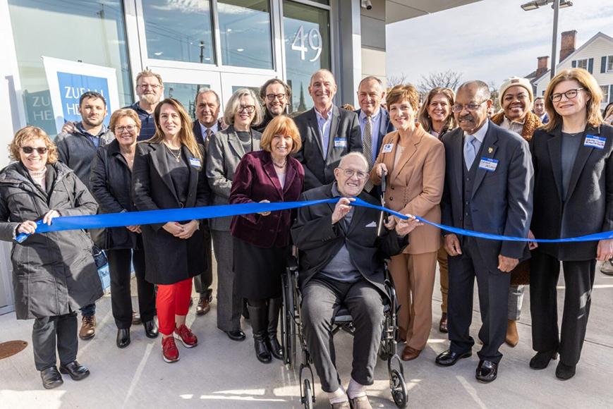 Group of people cutting a ribbon in front of a building